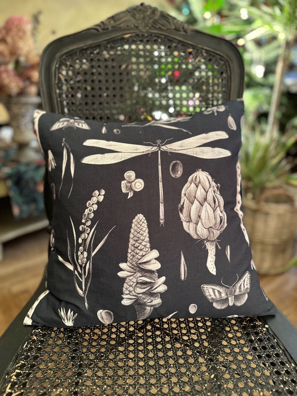 1. Decorative pillowcase with Seeds Carbon print featuring dragonflies and botanical elements on a black background, displayed on a vintage chair in a cozy setting