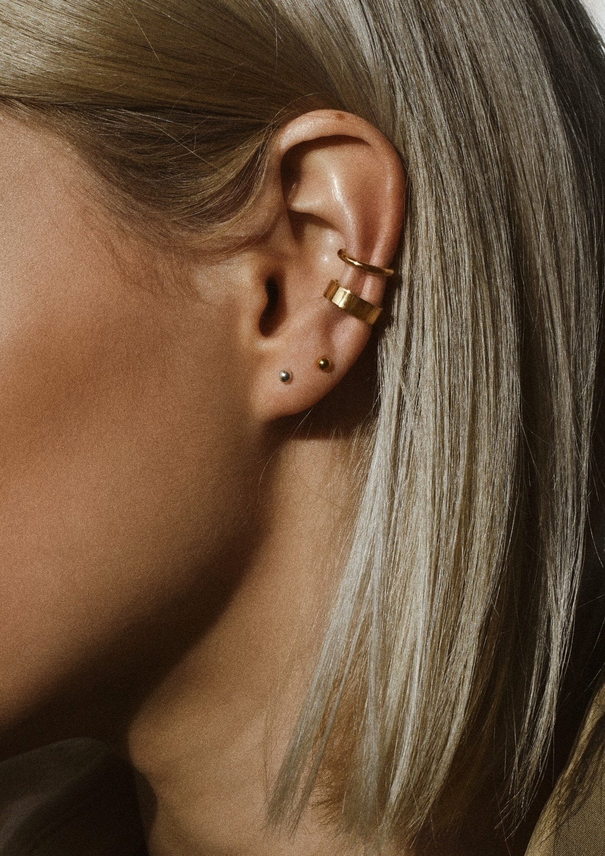 1. Women's gold pin-up earrings styled with multiple piercings, shown on model in lifestyle setting