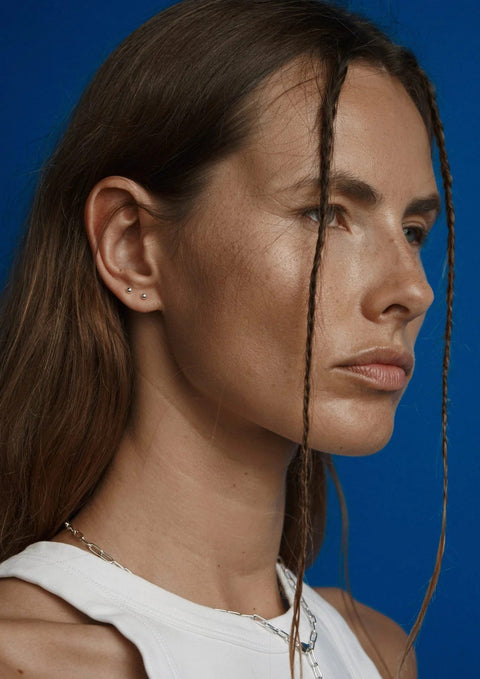 1. Woman wearing NO MORE Pin Up Earrings in sterling silver, showcasing elegant design against blue background
