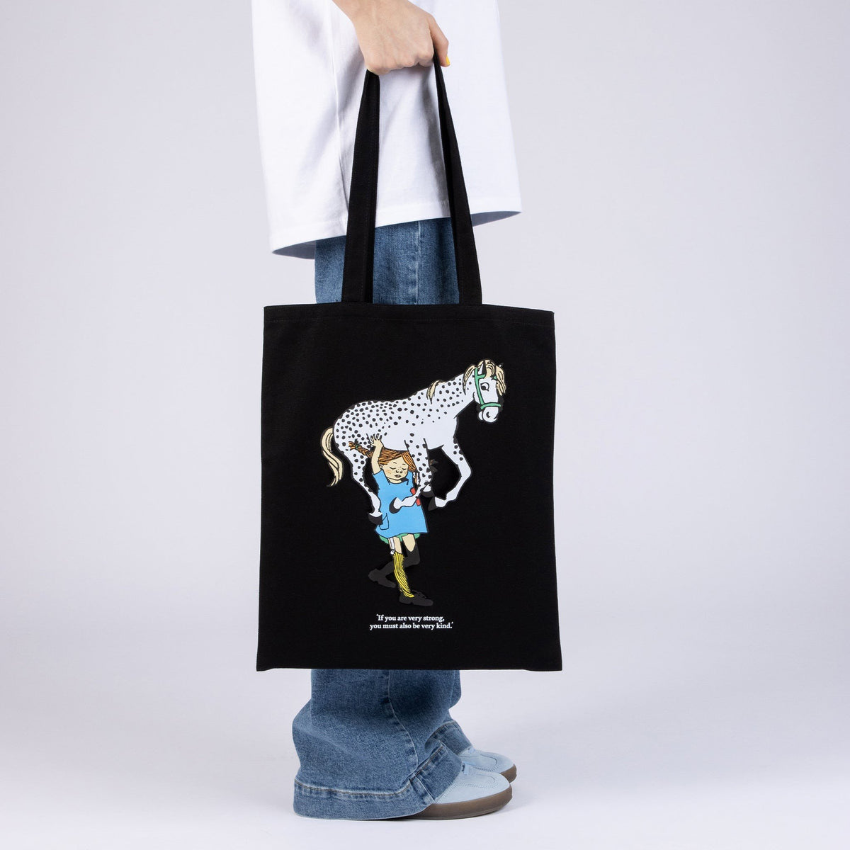1. Black Pippi Longstocking tote bag with horse design, held by model in casual outfit