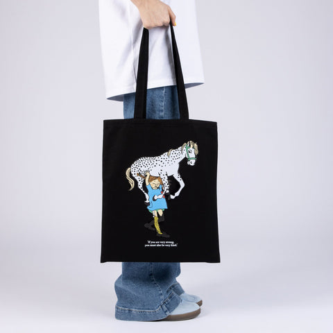 1. Black Pippi Longstocking tote bag with horse design, held by model in casual outfit