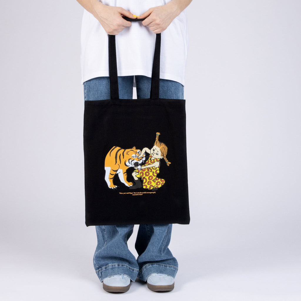 1. Black Pippi Tote Bag with tiger design, held by model in casual outfit, showcasing bold print and size
