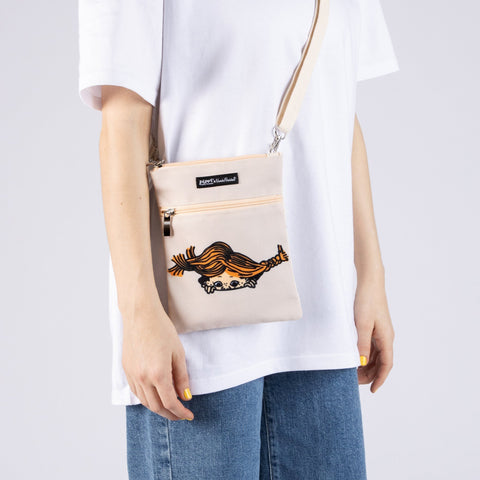 1. Women's Pippi Passport Bag in beige by Moomin, worn crossbody with casual outfit in studio setting