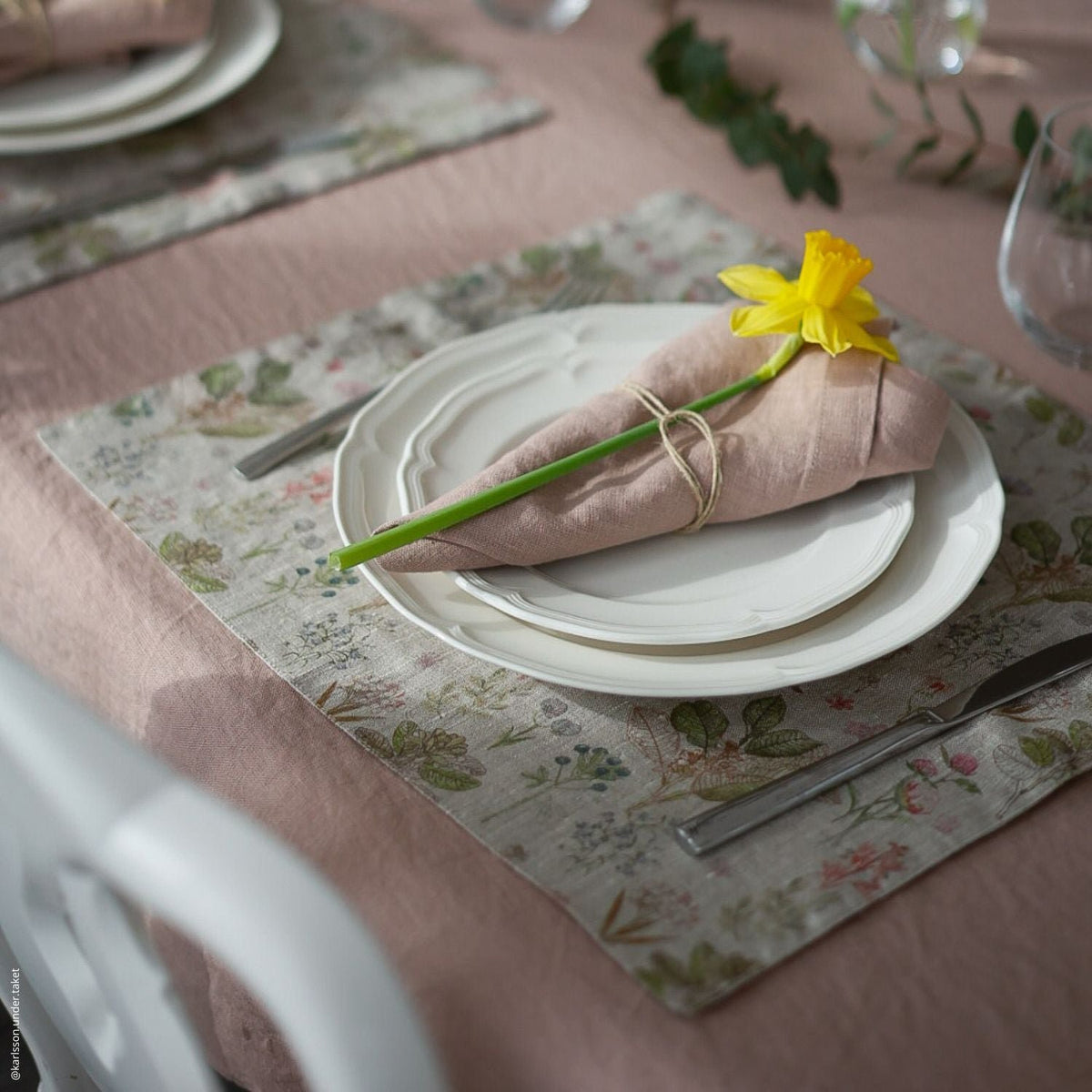 1. Dining table setting with floral linen placemat, white plates, pink napkin, and yellow flower