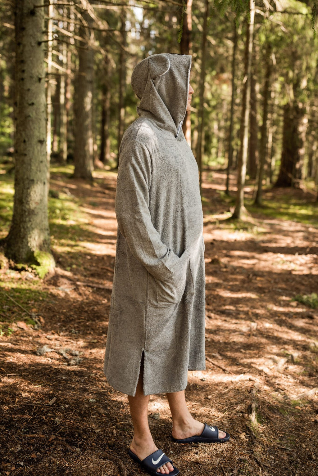 2. Side view of RÄTT Long-Sleeve Poncho KOALA in light grey, worn by a model in a forest setting