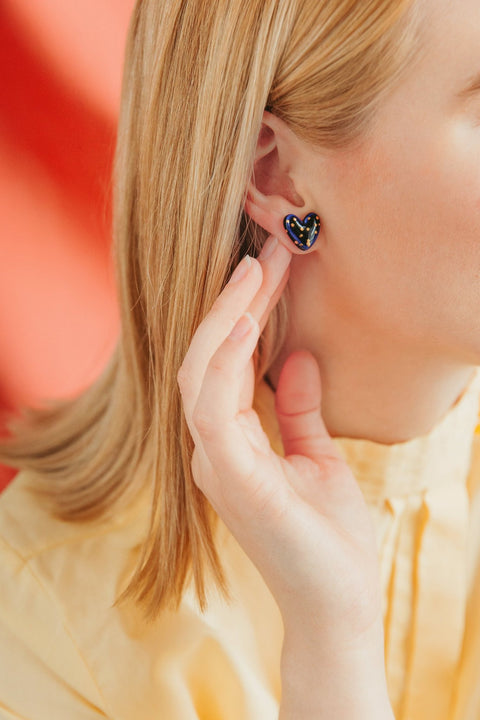1. Woman wearing Rozenthal blue dotted porcelain heart studs with 24k gold accents, shown in lifestyle setting