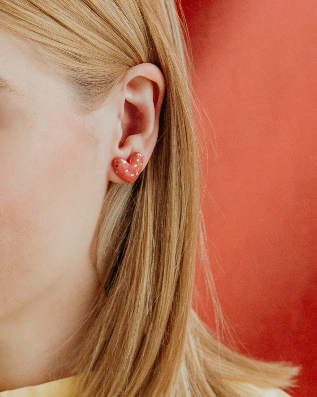 2. Close-up of Rozenthal pink dotted porcelain heart stud earring with 24k gold accents worn by a woman