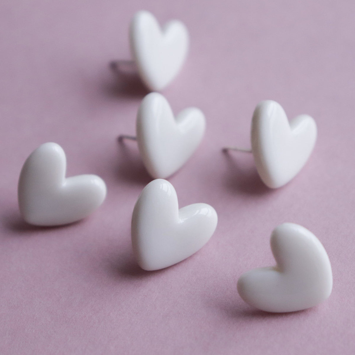 7. Flat lay of Rozenthal Porcelain Heart Studs in white, showing multiple pairs on pink background