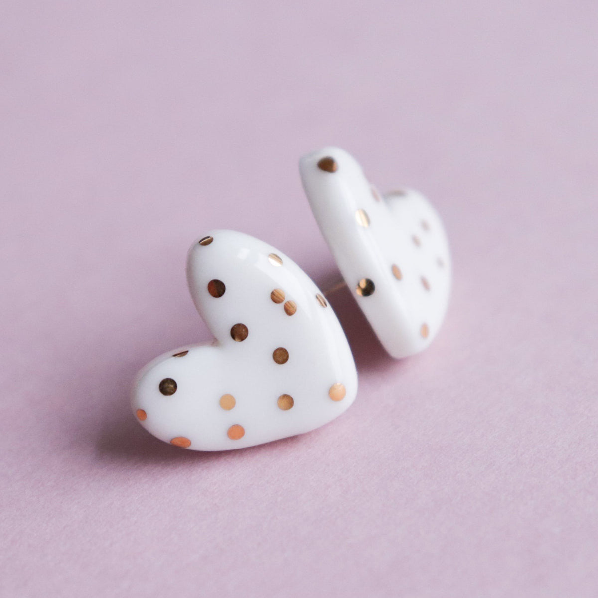 6. Side view of Rozenthal dotted porcelain heart studs with 24k gold accents, displayed on pink background