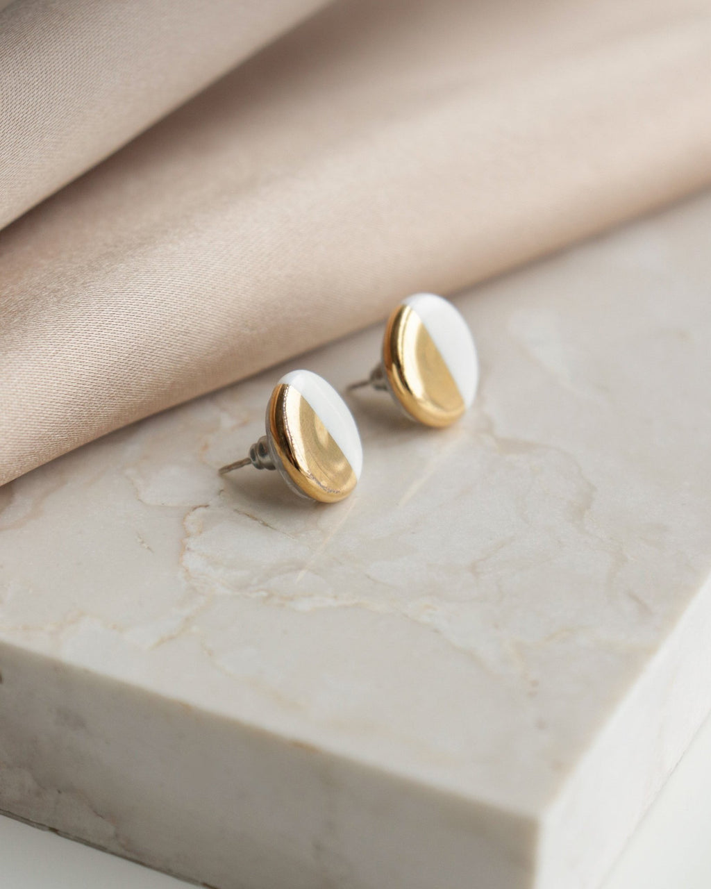3. Close-up of Rozenthal porcelain round stud earrings in white and gold on marble surface