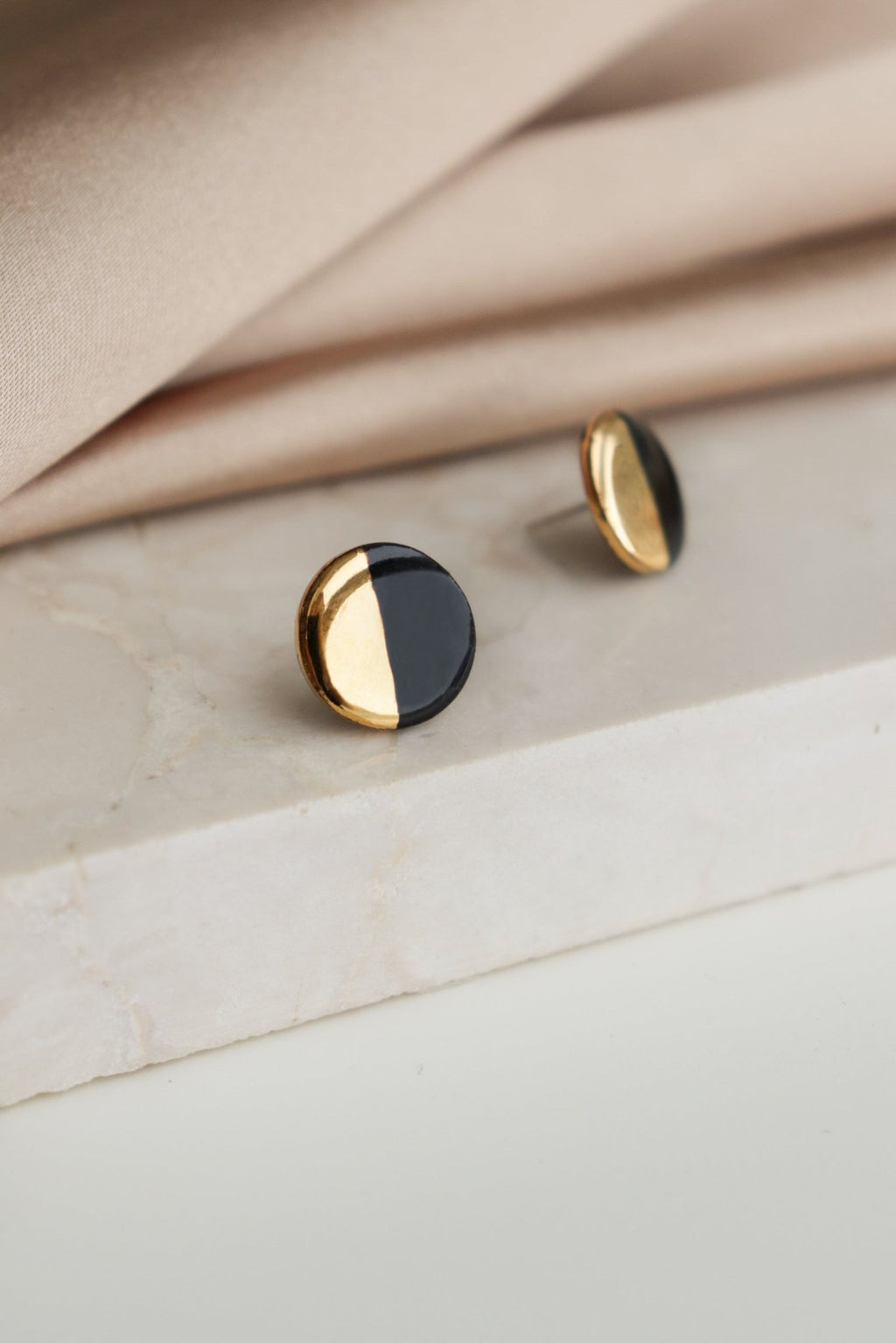 3. Close-up of Rozenthal black and gold porcelain round stud earrings on marble surface