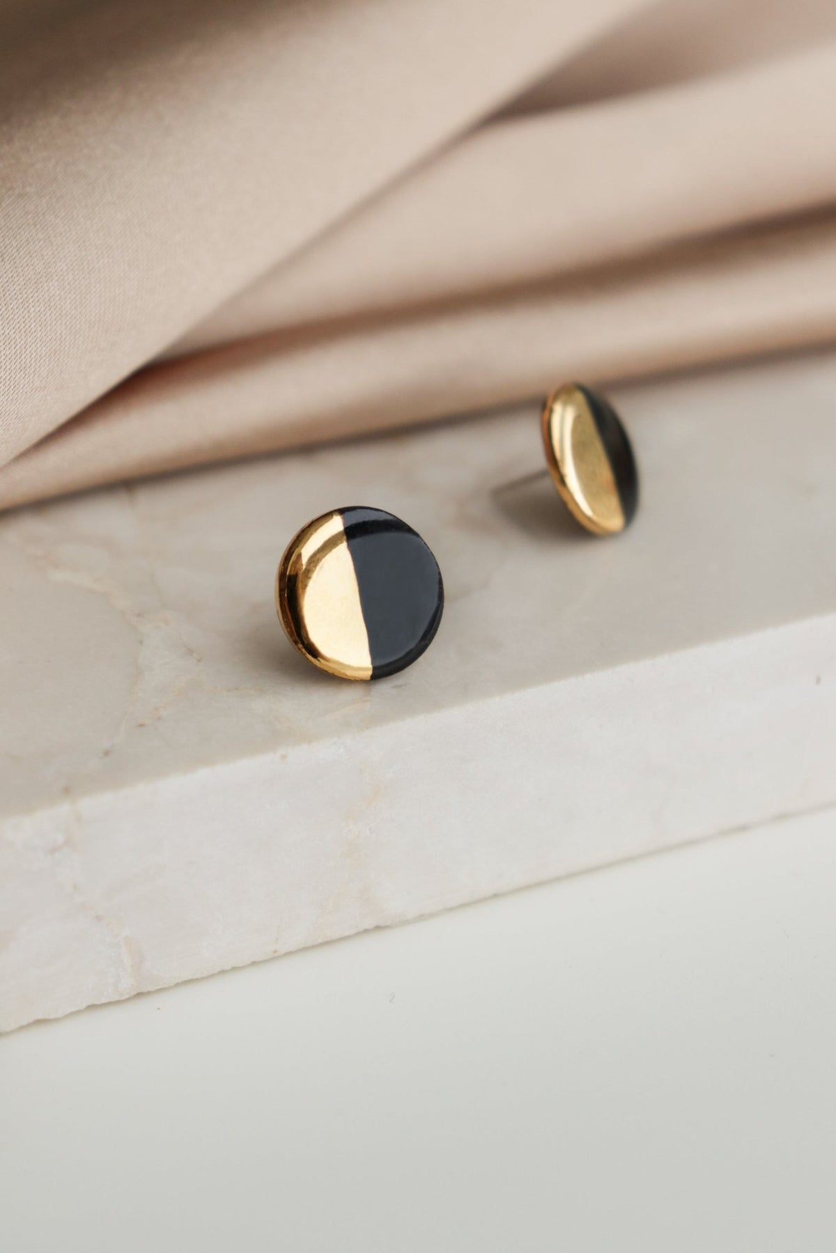 3. Close-up of Rozenthal black and gold porcelain round stud earrings on marble surface