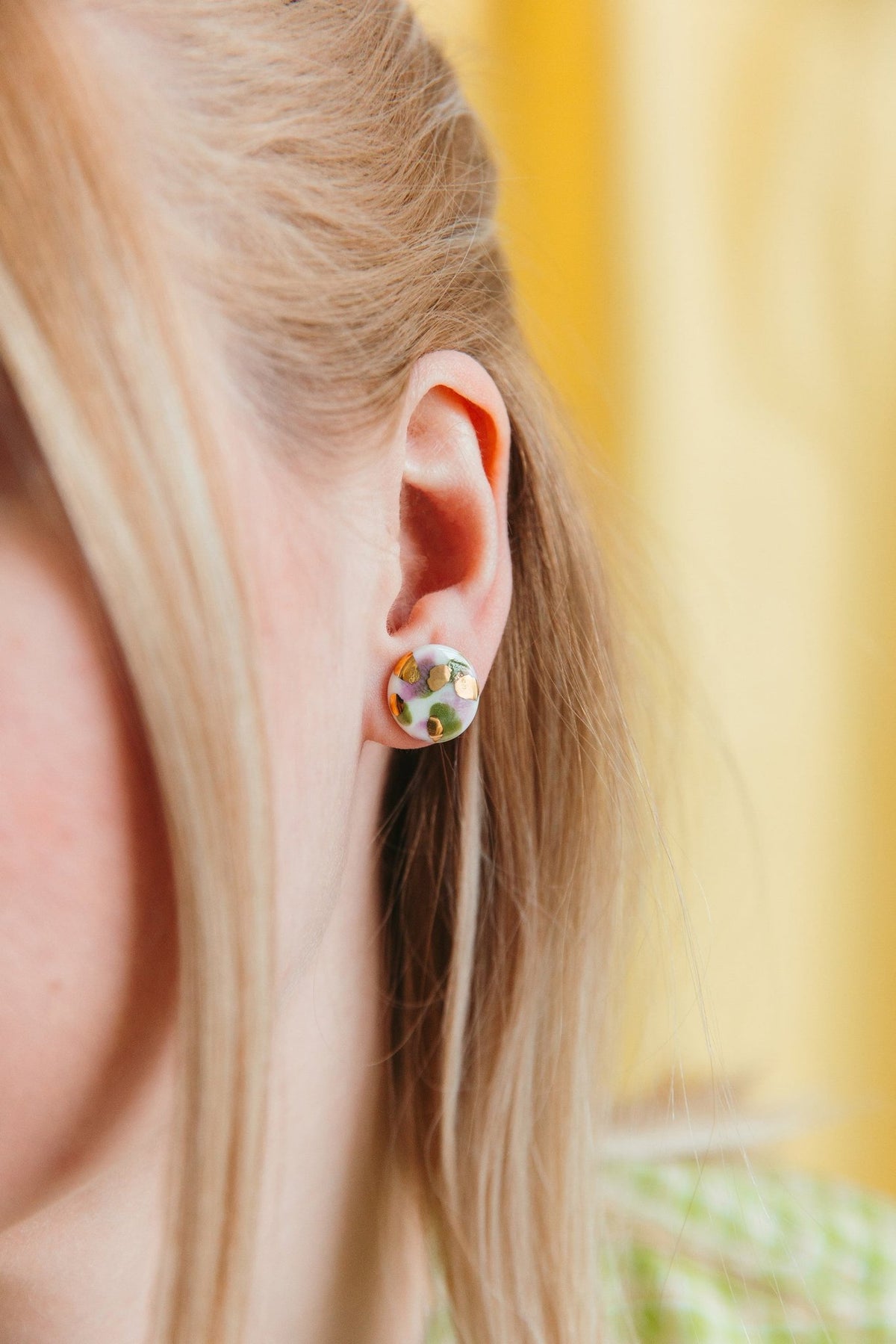1. Woman wearing Rozenthal Porcelain Tache Studs in green and orange, showcasing hand-painted design with 24k gold accents