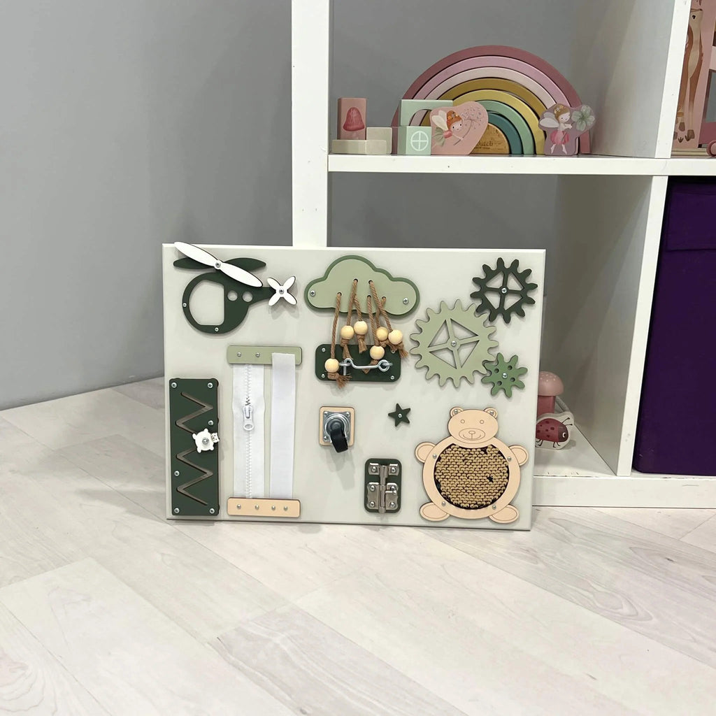1. Baby sensory busy board with green and beige elements placed on a light wooden floor near a shelf