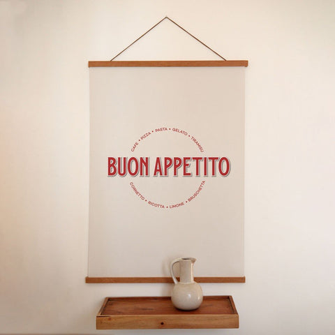 1. Minimalist Buon Appetito poster with red Italian typography hanging on a white wall above a wooden shelf with a ceramic jug, creating a rustic interior vibe