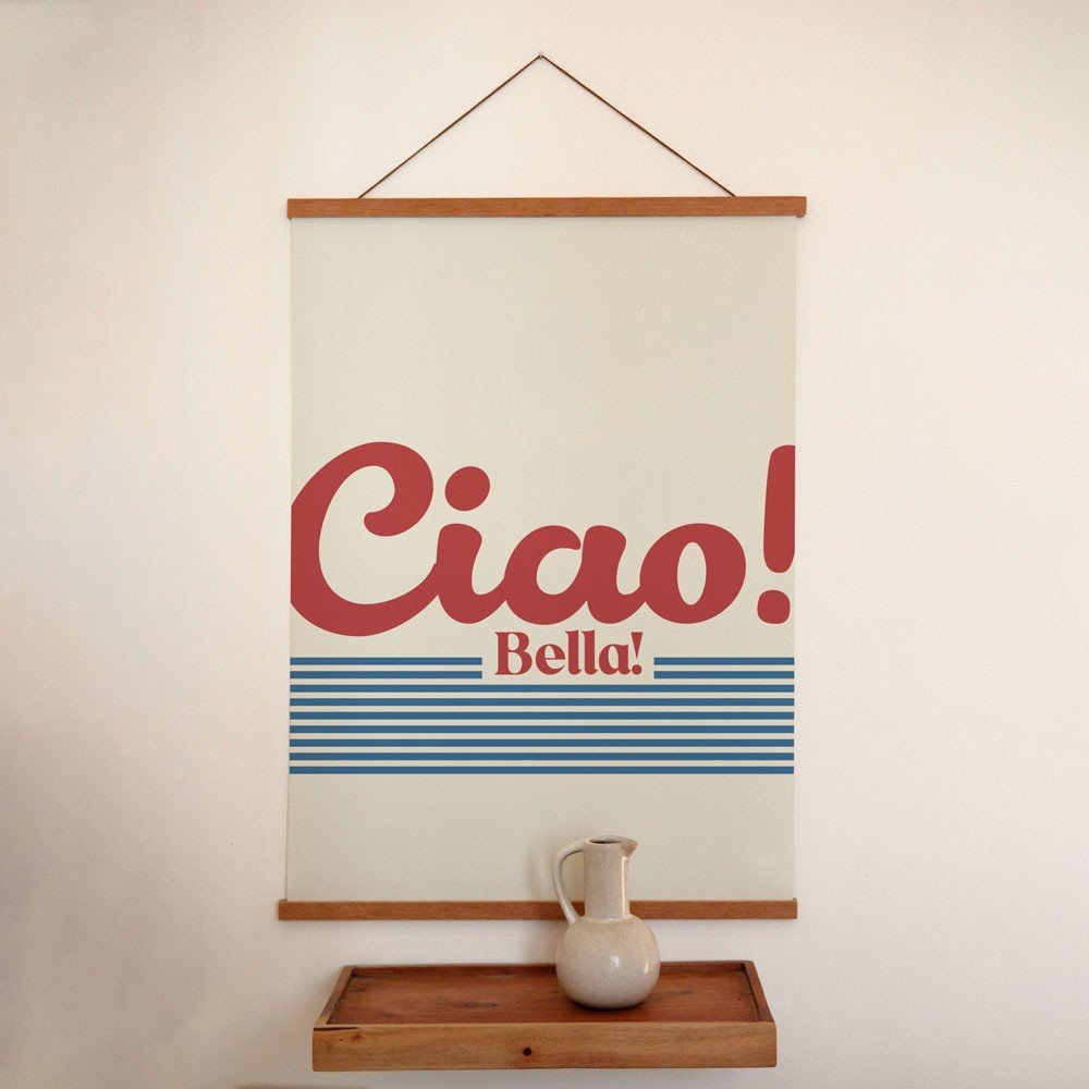 2. 'Ciao Bella' poster with red text and blue stripes on a minimalist wall above a wooden shelf with a ceramic jug