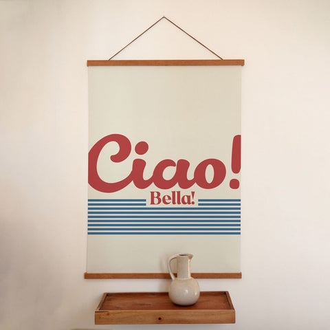 2. 'Ciao Bella' poster with red text and blue stripes on a minimalist wall above a wooden shelf with a ceramic jug
