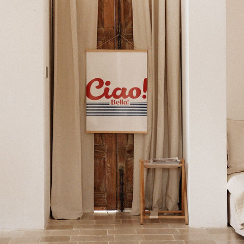 4. 'Ciao Bella' poster with red and blue typography hanging on a wooden door surrounded by beige curtains