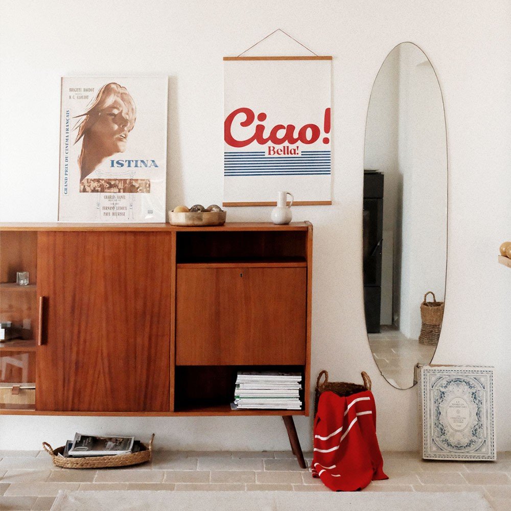 3. 'Ciao Bella' poster with red and blue design hanging above a mid-century cabinet in a stylish living room