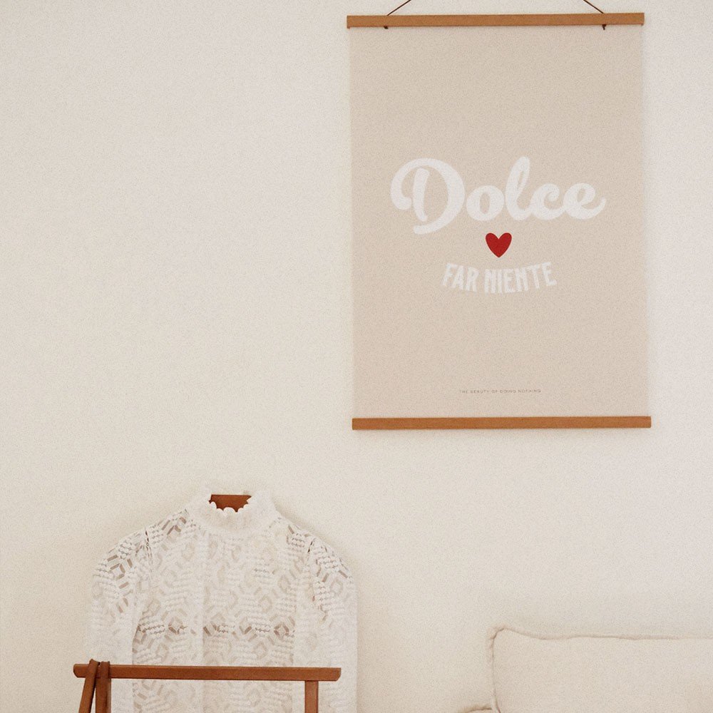 3. Close-up of beige 'Dolce far Niente' poster with white text and red heart, hanging above a lace garment on a wooden hanger