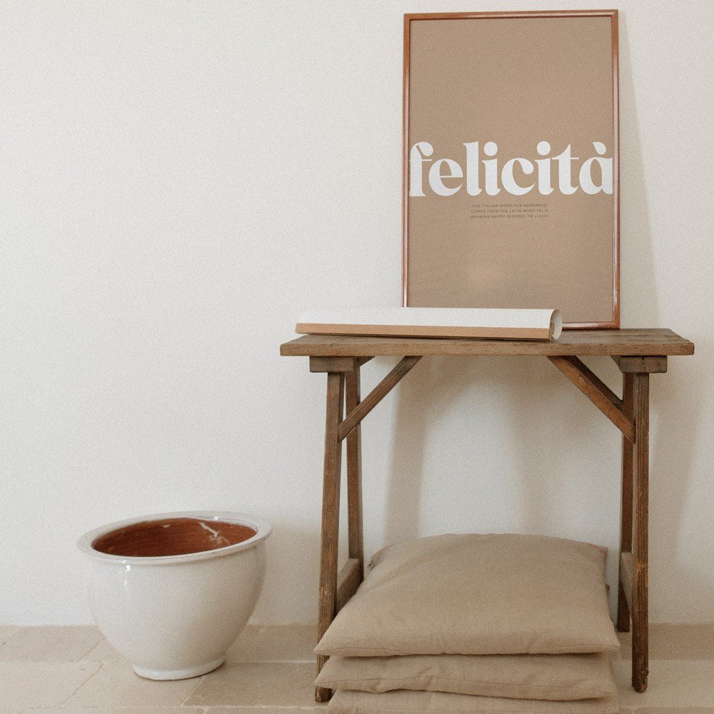 3. Terra Mamma Felicita poster with Italian typography on wooden table next to ceramic pot and cushions