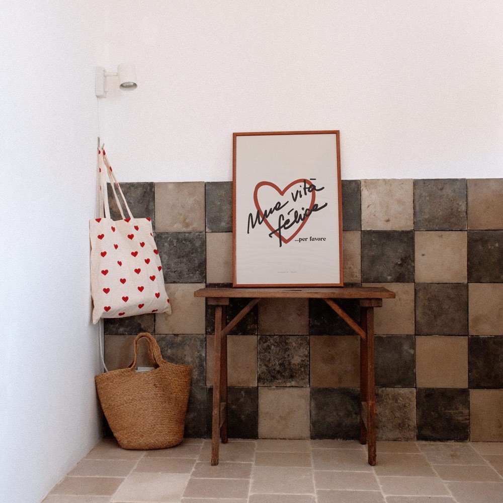 2. Framed Terra Mamma Vita Felice poster on wooden table against tiled wall, next to heart-patterned tote bag