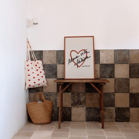 2. Framed Terra Mamma Vita Felice poster on wooden table against tiled wall, next to heart-patterned tote bag