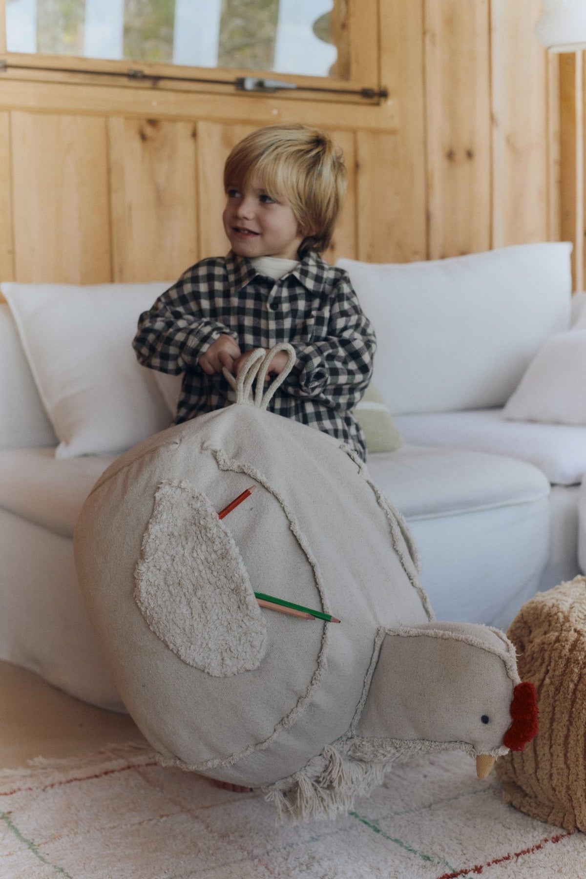 1. Child holding beige chicken pouf by handle in wooden interior room
