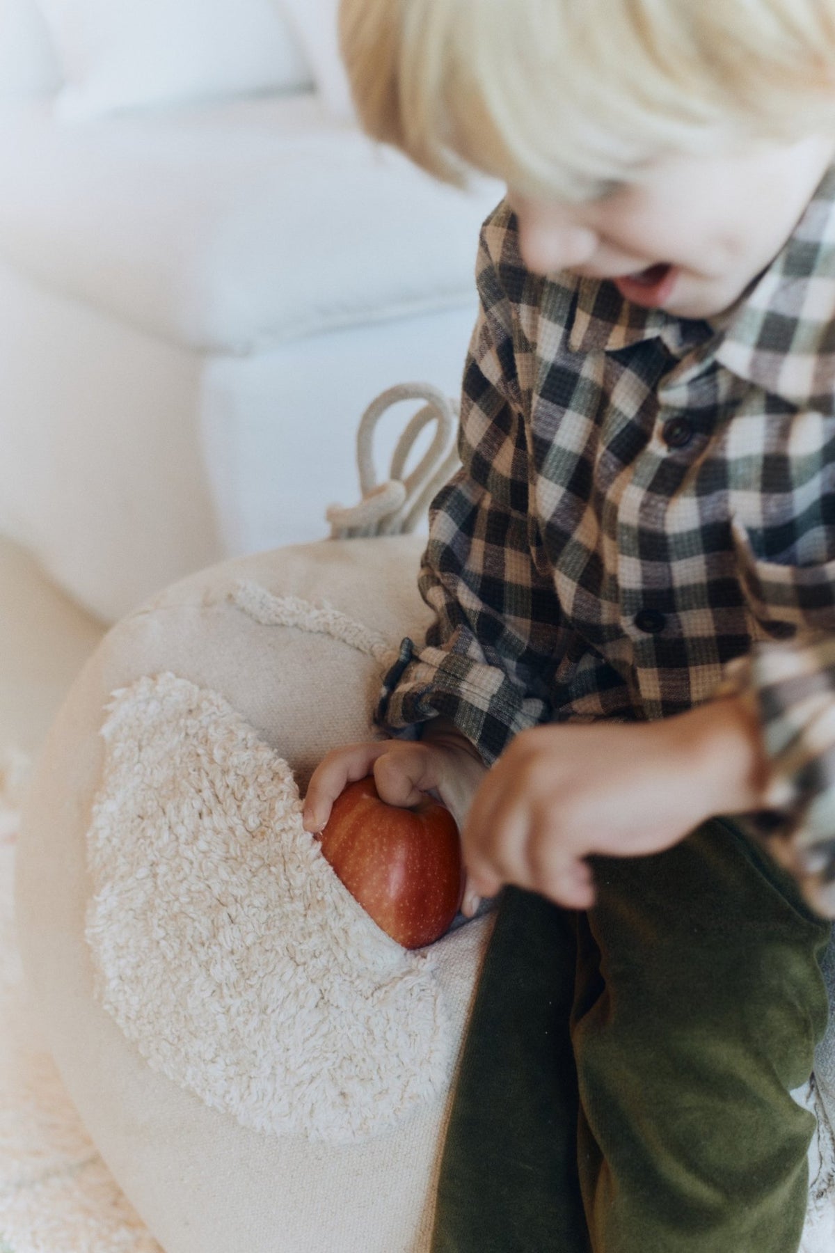 3. Close-up of child placing apple on beige chicken pouf with textured wing detail