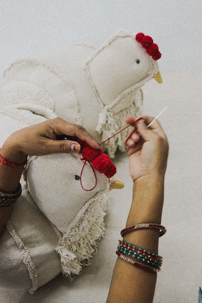 3. Close-up of hands crafting red comb on beige chicken pouf