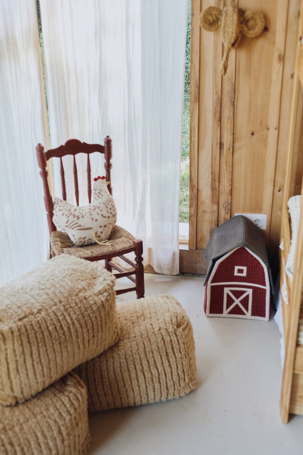 1. Rustic interior with Lorena Canals Pouf Haystack in light honey, placed near a wooden chair and toy barn, enhancing a cozy, country-style room