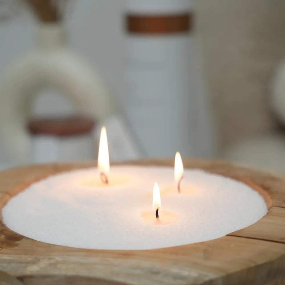 3. Close-up of three lit wicks in white candle sand in wooden container
