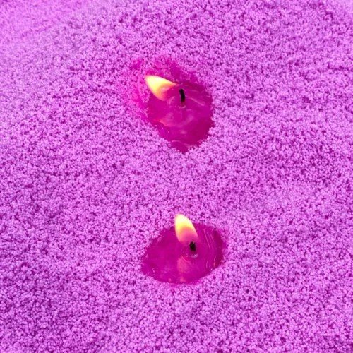 1. Two lit wicks in deep amethyst powdered candle sand creating a warm glow