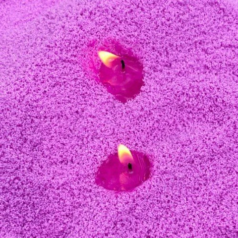 1. Two lit wicks in deep amethyst powdered candle sand creating a warm glow