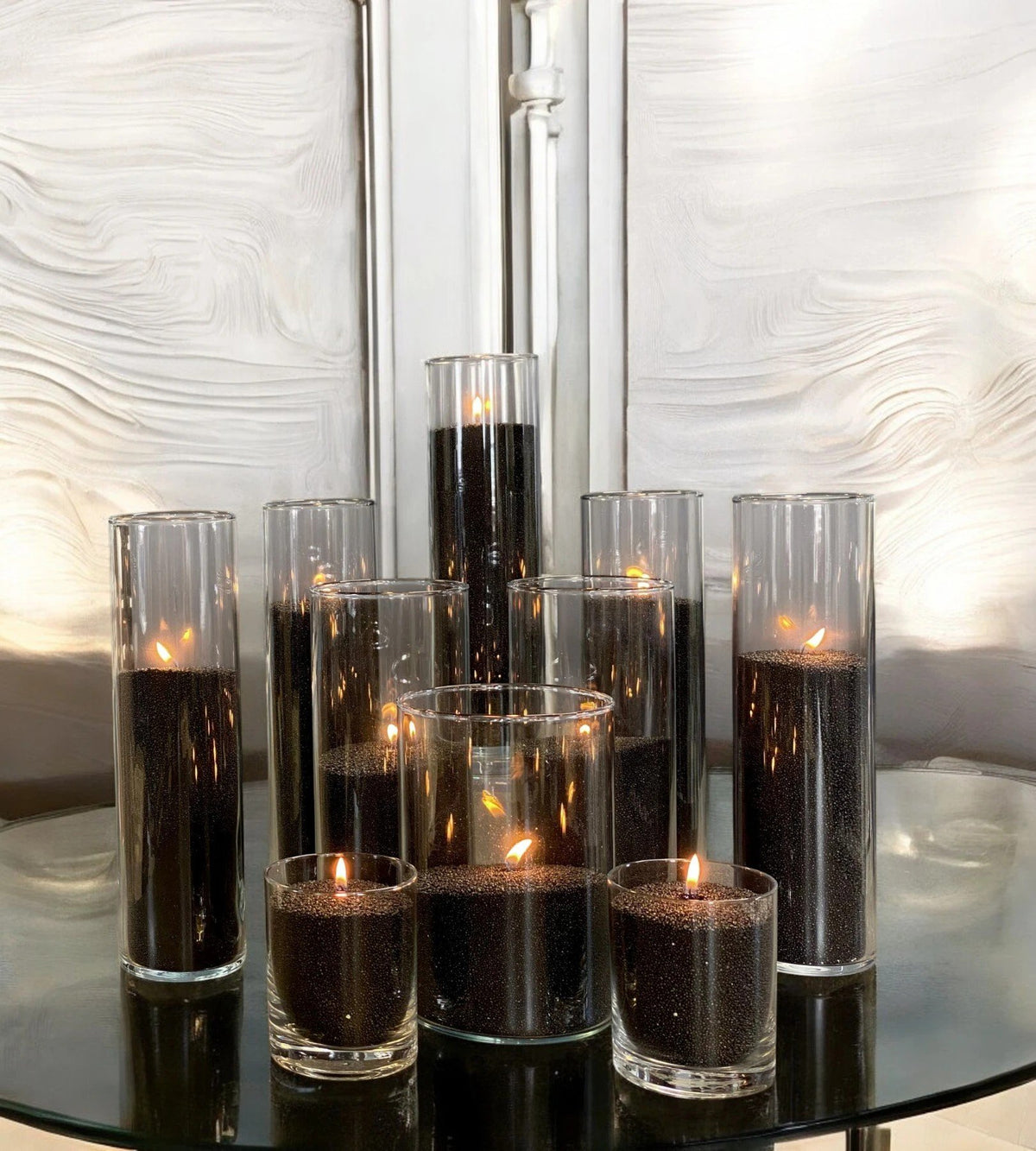1. Multiple glass containers with black powdered candles lit, creating a warm ambiance on a reflective surface