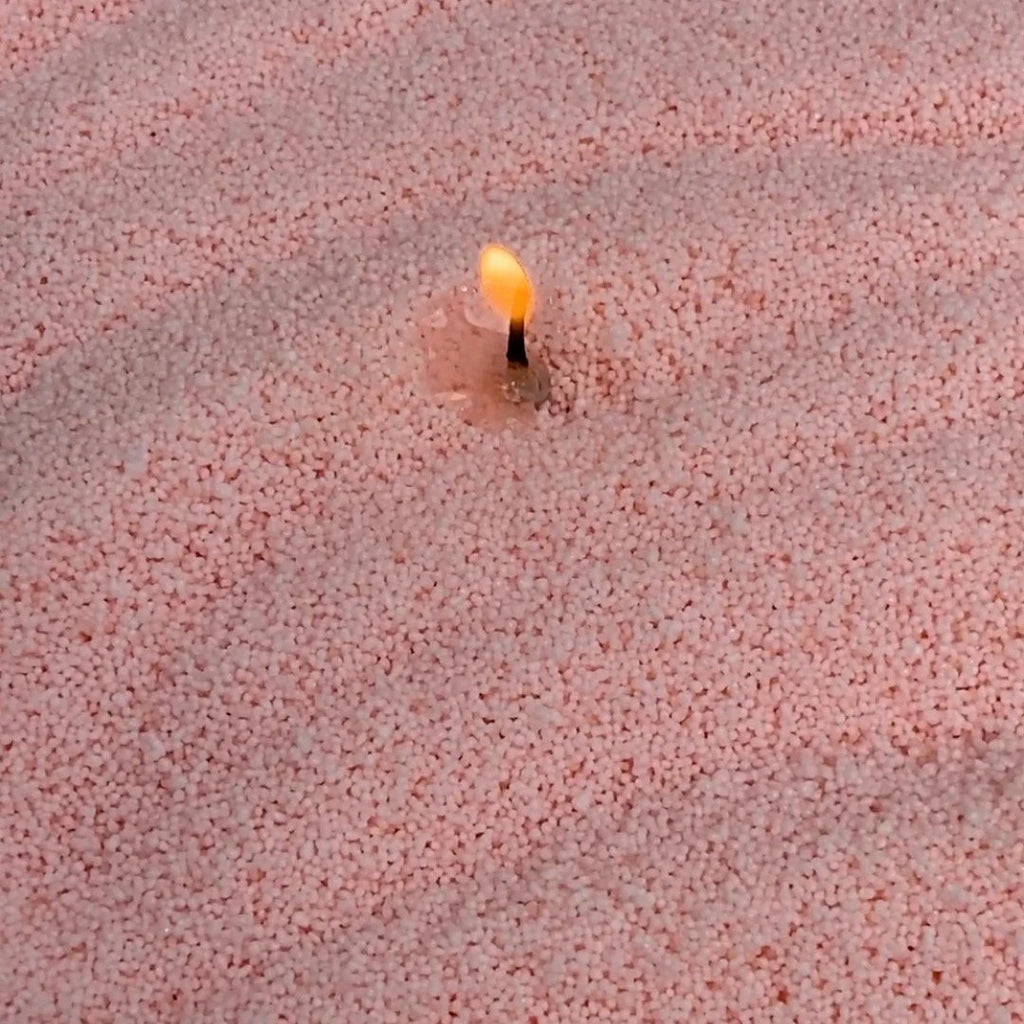 3. Close-up of lit wick in creamy peach candle sand showing texture and flame