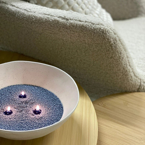 1. Three lit wicks in a bowl of dark blue Candledust on a wooden table, cozy setting with a textured blanket