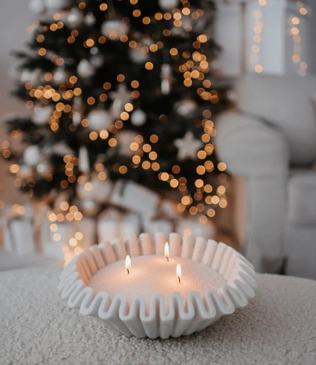 1. Ivory powdered candle in decorative bowl with three wicks, set on table with blurred Christmas tree lights in background