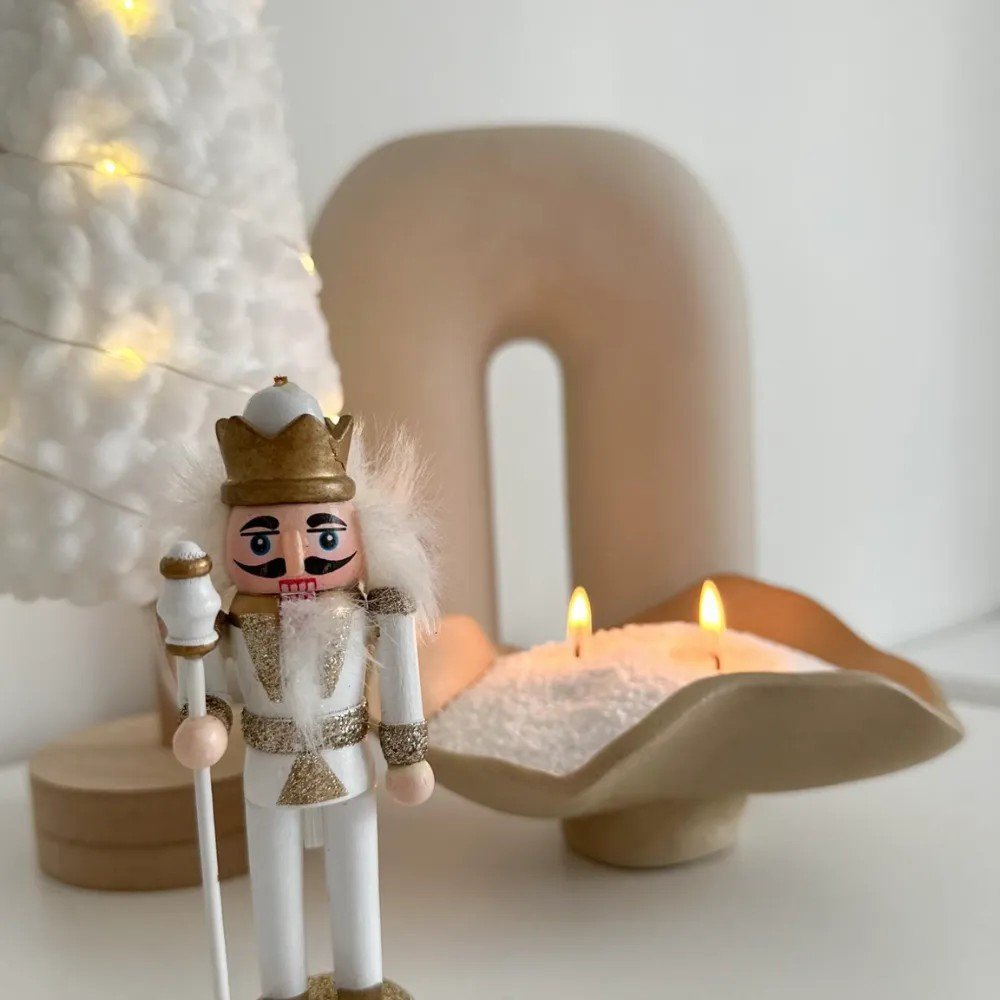 1. Ivory powdered candle in unique holder with two wicks, next to nutcracker and decorative tree, on light surface
