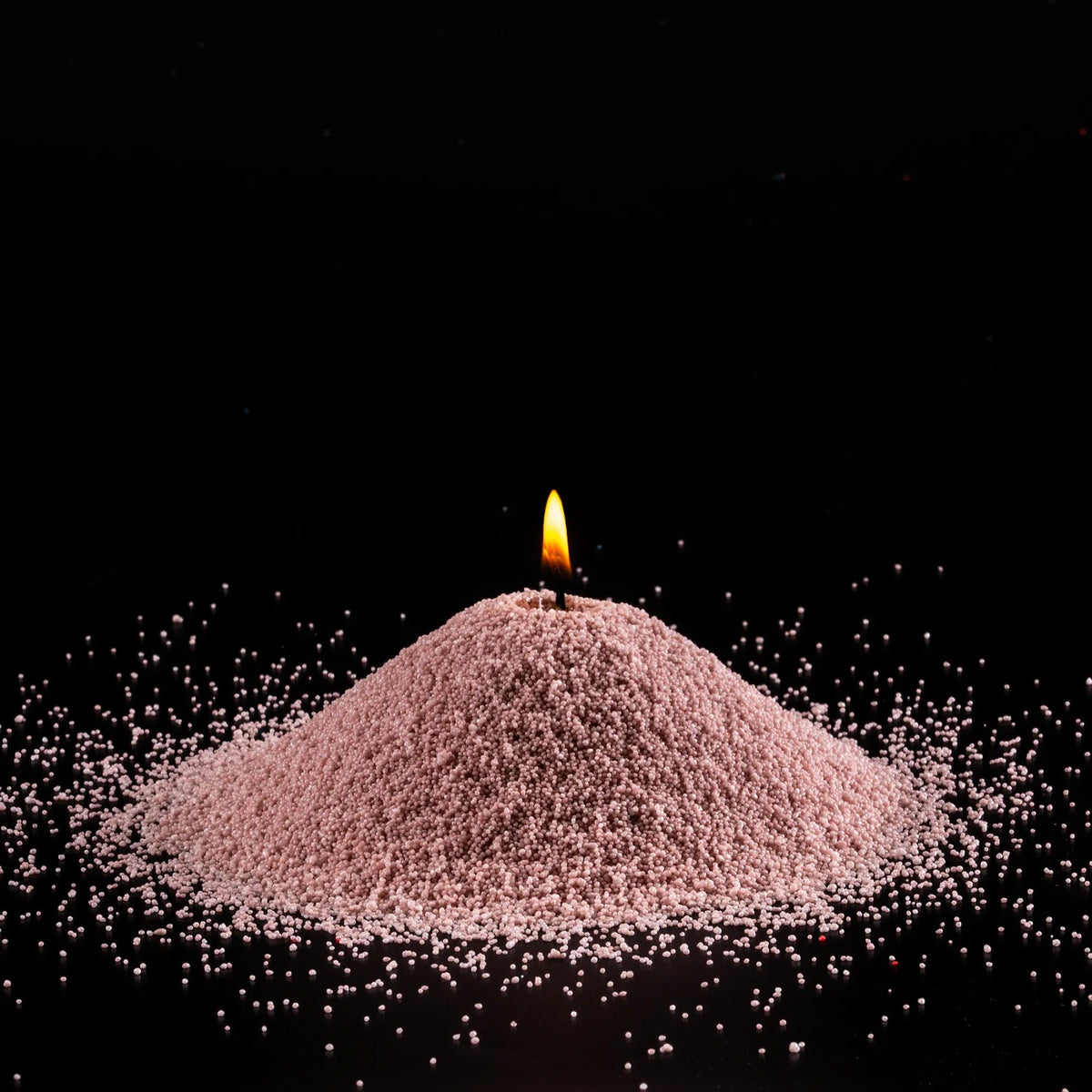 2. Burning pile of nude-colored candle sand on black background