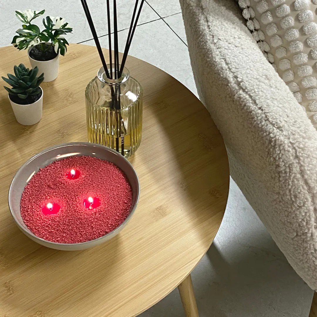 5. Raspberry candle sand with three lit wicks in bowl on wooden table next to decor items