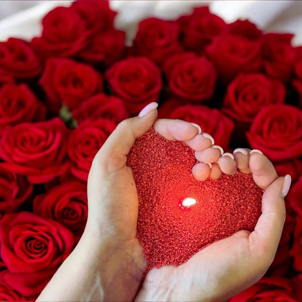 1. Hands holding heart-shaped red candle sand with lit wick, surrounded by red roses