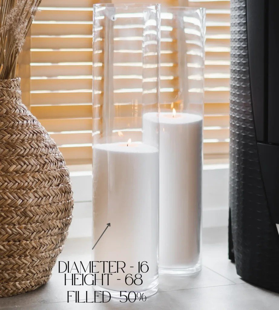 1. Two tall glass vases filled with white candle sand, lit wicks, placed near a woven basket and window blinds