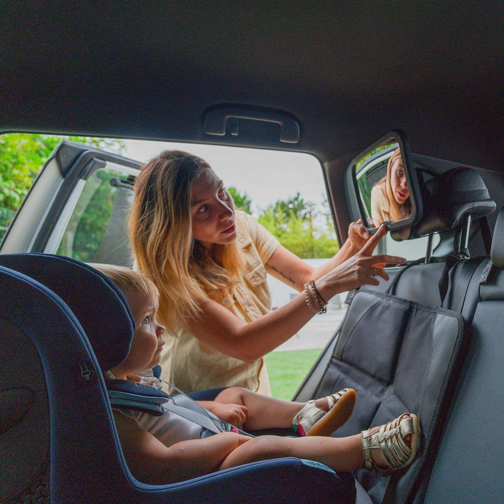 1. Woman adjusting rearview mirror with child in car seat, using Ezimoov car seat protector in backseat