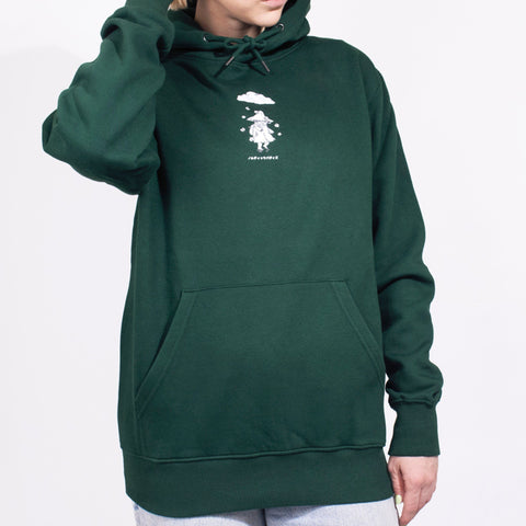 1. Female model wearing green unisex hoodie with Moomin character print, hand on head, in studio setting