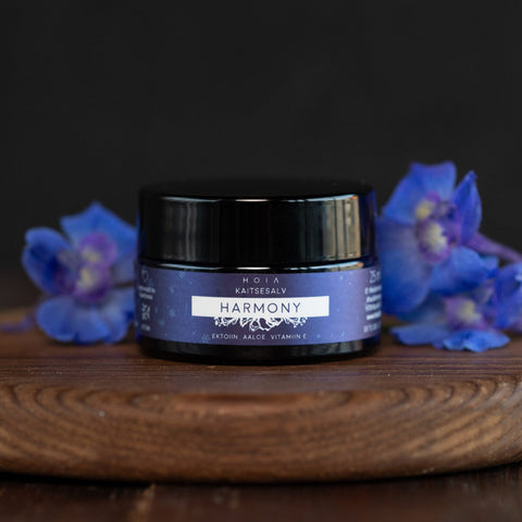 2. HOIA homespa Protective Balm Harmony in a dark jar with blue label, surrounded by blue flowers on a wooden surface