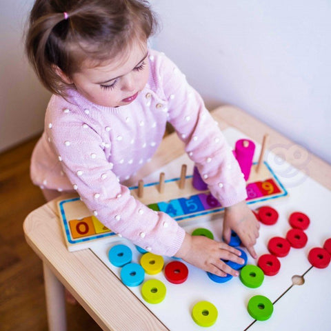 4. Child in pink polka dot sweater arranging colorful rings on a wooden counting puzzle