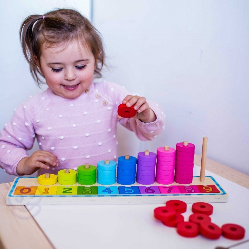 14. Child in pink polka dot sweater stacking red rings on a colorful wooden counting puzzle