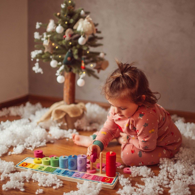 1. Child in pink pajamas playing with colorful wooden counting puzzle under a decorated Christmas tree