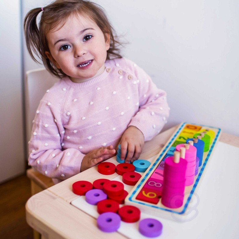 13. Child in pink polka dot sweater playing with colorful wooden counting puzzle at a table